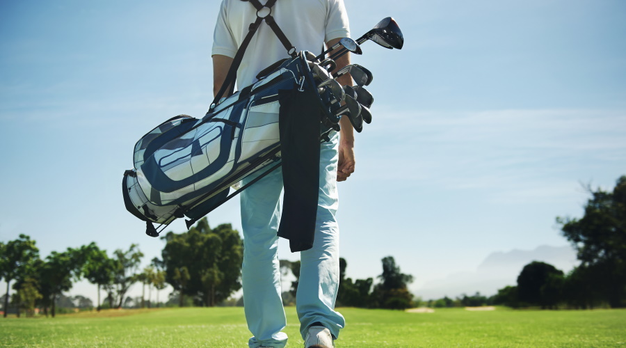 Golf man walking with shoulder bag on course in fairway