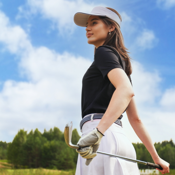 golfer holding golf club on field and looking away standing on golf course on a sunny day.