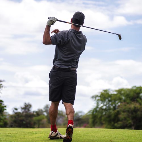 golfer in golf shorts hitting a golf shot on the golf course - lower and improve your golf handicap